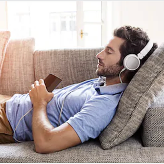 Man lying down on a couch wearing headphones,  having a remote Biofield Tuning Sound Healing session.
