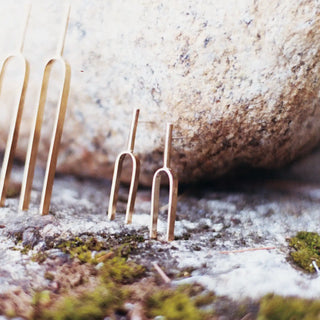 Small Handmade Tuning Fork Earrings in sterling silver and solid brass displayed on a natural stone surface.