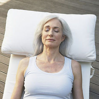 A woman receiving a sound healing session, lying down on a massage table with a pillow under her head with her eyes closed.
